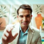 Confident businessman reaching towards camera in modern casual office setting.